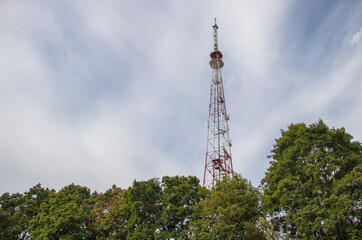 A tall, slender television tower stands against the backdrop of trees and sky