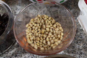 Ingredients to prepare chiles en nogada. White pine nuts in a glass bowl on a marble countertop. Close-up photography of pine nuts as an ingredient for cooking. 