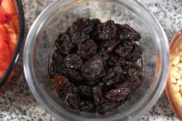 Ingredients to prepare chiles en nogada. Dried prunes in a glass bowl on a marble countertop. Close-up photography of prunes as an ingredient for cooking.