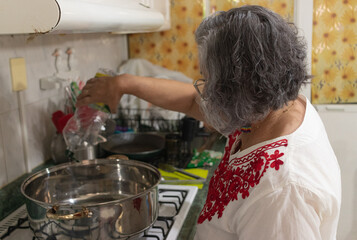 Mexican grandmother pouring oil into the ground beef stew to prepare the filling for chiles en...