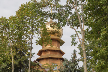 A wooden Russian Orthodox church with golden domes, surrounded by trees and greenery in the city