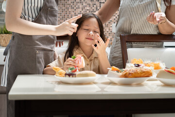 Happy little daughter eat bakery with family background in kitchen at home	