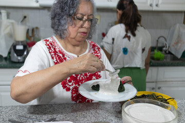 A woman in a red-embroidered blouse garnishes a chile en nogada with parsley and pomegranate seeds...