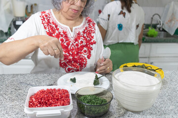 A woman in a red-embroidered blouse garnishes a chile en nogada with parsley and pomegranate seeds...