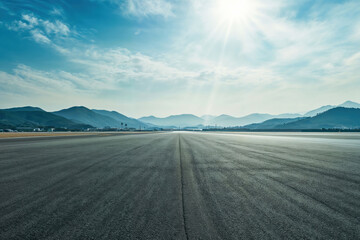 Empty runway going towards mountains under a beautiful blue sky with a shining sun