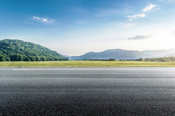 Empty asphalt road is leading to beautiful green mountains in the distance with under blue sky background
