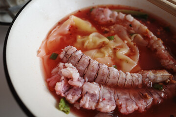 A close-up shot of a mantis shrimp served in a vibrant, spicy soup. 