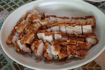 A close-up shot of succulent crispy pork belly, sliced and arranged on a white plate.