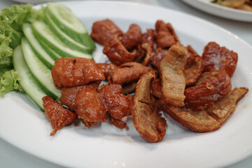 A plate of grilled pork intestines served alongside fresh basil, cucumber, and a spicy dipping sauce. 