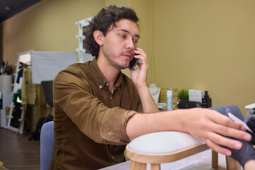 A man in a salon receives nail care while on a phone call, blending modern life with beauty