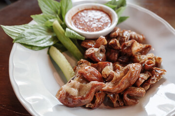 A plate of grilled pork intestines served alongside fresh basil, cucumber, and a spicy dipping sauce. 