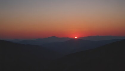 A silhouette of a mountain range with the setting sun peeking over the top of a peak.