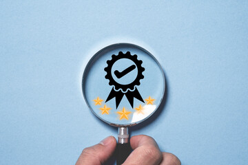 Businessman holding magnifier glass with the best quality assurance and golden five stars for focus...