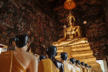 A serene image of a large golden Buddha statue inside a beautifully adorned Thai temple. In the...