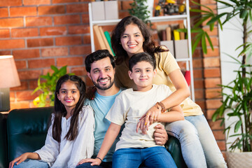 Cheerful Indian parents and kids sitting on the sofa, enjoying playful moments and laughter at home