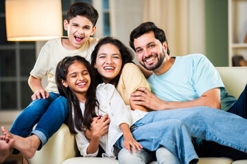 Fototapeta premium Cheerful Indian parents and kids sitting on the sofa, enjoying playful moments and laughter at home