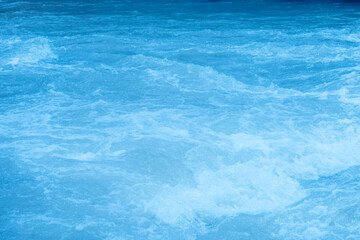 Blue water with ripples on the surface. Defocus blurred transparent blue colored clear calm water surface texture with splashes and bubbles. Water waves with shining pattern texture background.