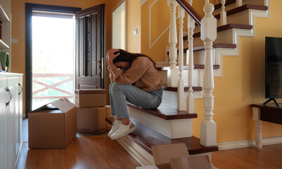 Divorced woman sitting on the stairs of her home, looking sad and exhausted. Surrounded by moving...