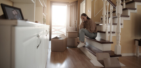 Divorced woman sitting on the stairs of her home, looking sad and exhausted. Surrounded by moving...