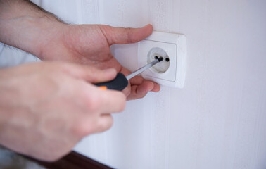 Close-up shot of a person using a screwdriver to repair or install a wall electrical socket. The...