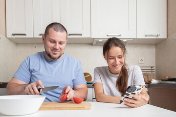 Teenage girl and father cook using a recipe on phone, preparing a meal together, experiencing the joy of cooking and family love.