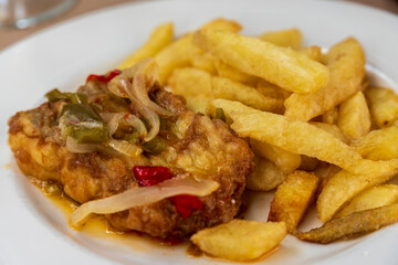 Fried hake fish with onion and fries on plate Spain