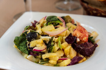delicious new potato salad with red onion, capers, greens in a black bowl, horizontal view from above, copy space