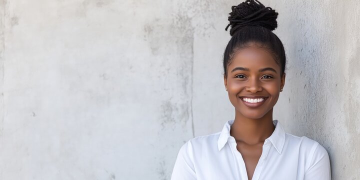 A smart young smiling black businesswoman standing in front of a white weathered concrete wall