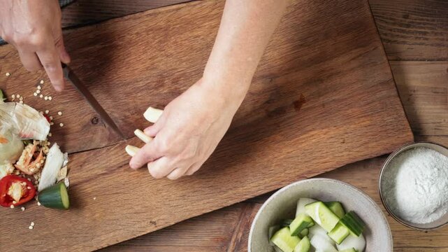 Chef cuts a garlic with a knife on a wooden kitchen board for healthy dinner, top view. Process of making gazpacho soup