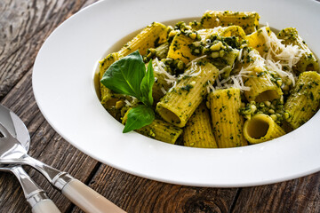 Pasta with basil pesto sauce and parmesan served in white bowl on wooden table

