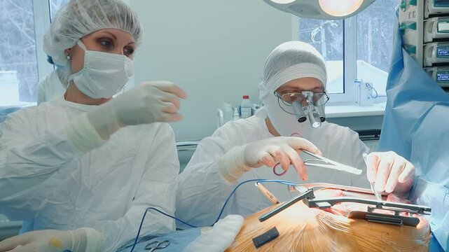 Assistant gives forceps to doctor in surgery room. Surgeon conducts artery bypass surgery with nurse help in hospital. Heart disease treatment