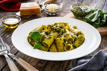 Pasta with basil pesto sauce and parmesan served in white bowl on wooden table
