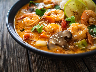 Tom Yam Kung soup - Thai soup with shrimps and rice noodles served in black bowl with chopsticks on wooden table
