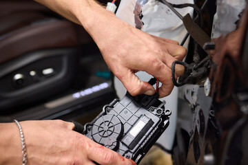 A mechanics hands are seen repairing the cars interior door panel controller inside the vehicle