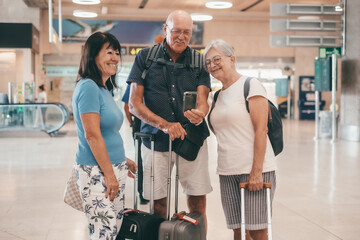Group of senior happy people in airport departure area waiting to board flight. Travel and tourism concept, carefree people with luggages and backpack