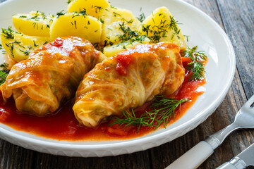 Wrapped minced meat in cabbage leaves served in tomato sauce with boiled potatoes on white plate on wooden table - polish dish golabki