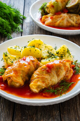 Wrapped minced meat in cabbage leaves served in tomato sauce with boiled potatoes on white plate on...