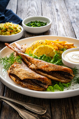 Fried sea bass served on lettuce with French fries, lemon and mayonnaise on white plate on wooden table
