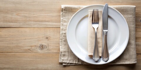 Place setting with stainless steel knife, fork and plate on a white cloth napkin