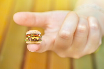 Hand holding a very small hamburger. Background on the topic of high prices for food and groceries. Small portions in fast food.