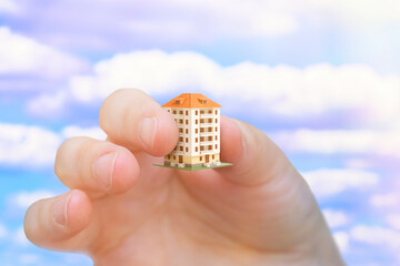 A hand holding a very small residential house. Background on the topic of utility prices and building maintenance. House sizes on the real estate market.