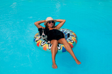 Pretty young woman lounging in the pool with her dog