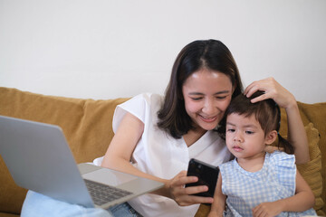 Woman working from home, multitasking with a laptop and smartphone while sitting on a couch with...