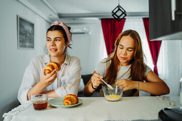 Two female friends or sisters are eating croissant for breakfast