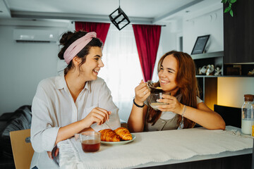 Two female friends or sisters are eating croissant for breakfast
