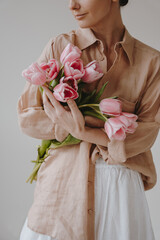 Elegant simplicity. Person in beige and white holding a vibrant bouquet of pink tulips against a...