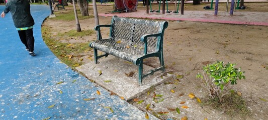 Bird poop on dark green metal bench in park beside walkway in Thailand.