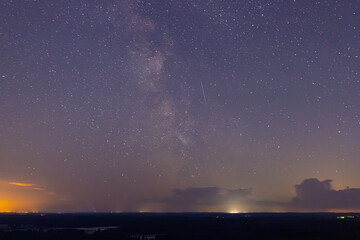 A mesmerizing long-exposure shot captures star trails swirling across the night sky above a brightly lit town. The sky fades from deep blue to purple, creating a stunning cosmic display over the dark