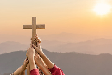 Friendship hands praying and holding Christian cross for worshipping God on mountain at sunrise background. Christian, Christianity, Religion copy space background. Easter Sunday concept: