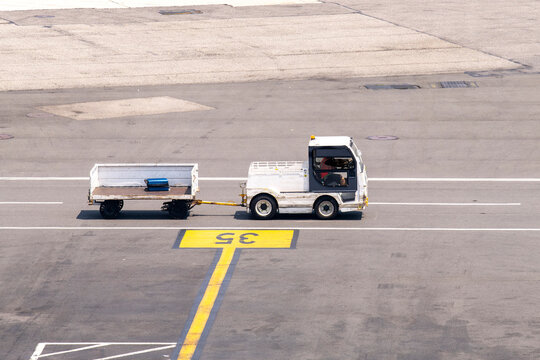 High angle view one baggage tractor-trailer (baggage tow tractor) on a service road on the tarmac of the airport with one suitcase on trolley